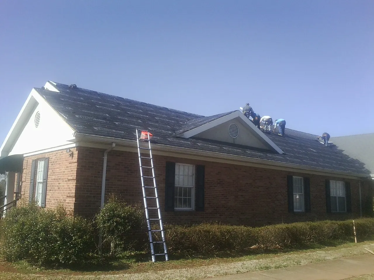 Crew tearing shingles off a brick ranch roof with a ladder set — Emergency Roof Repair work by our crew in Telford
