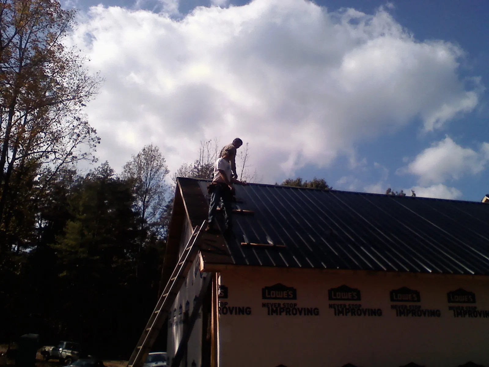 Roofer fastening dark metal panels high against a cloudy sky, from a Roof Inspection job in Telford