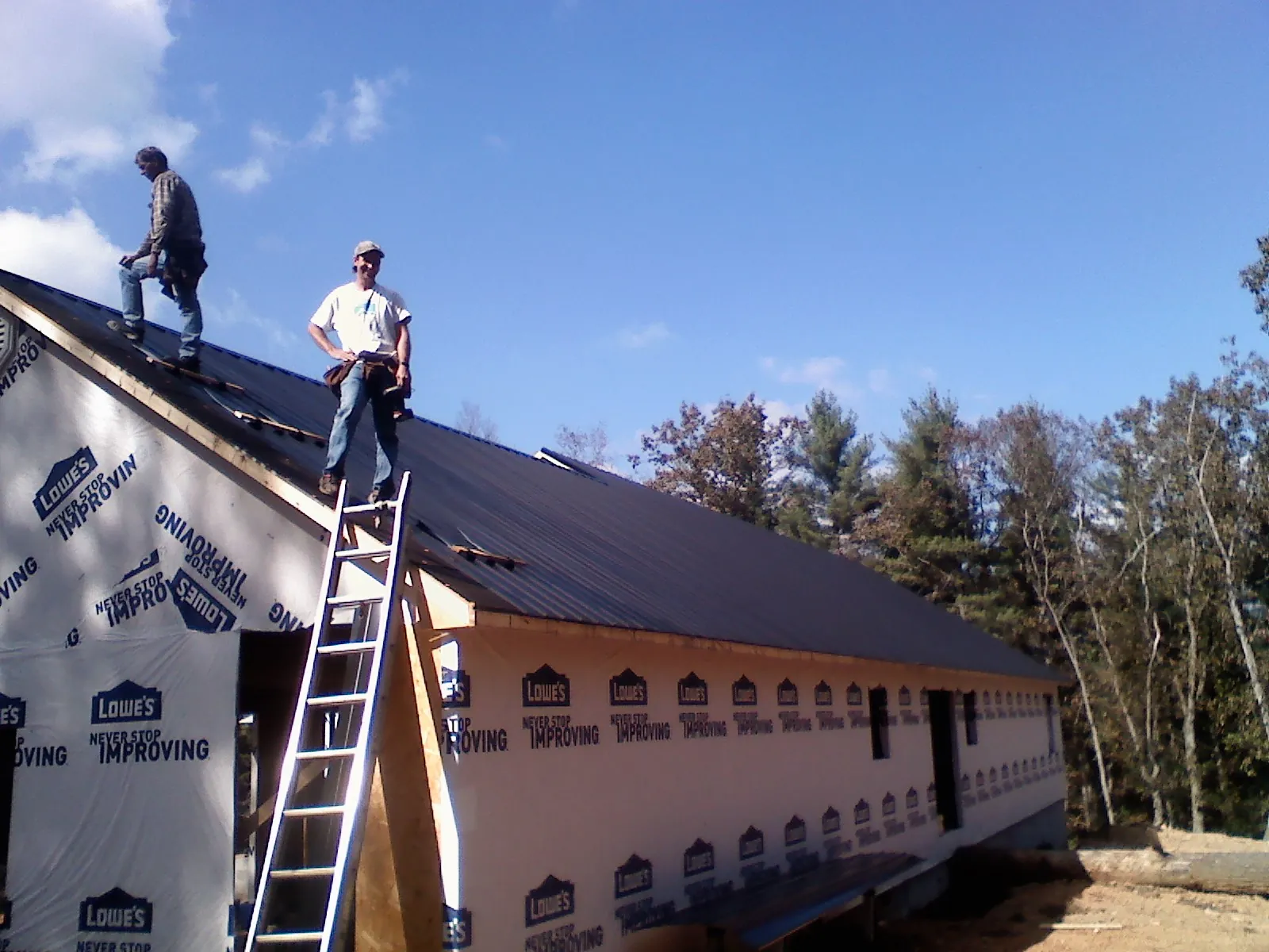 Two roofers standing on a long dark metal roof over a wrapped building in Telford